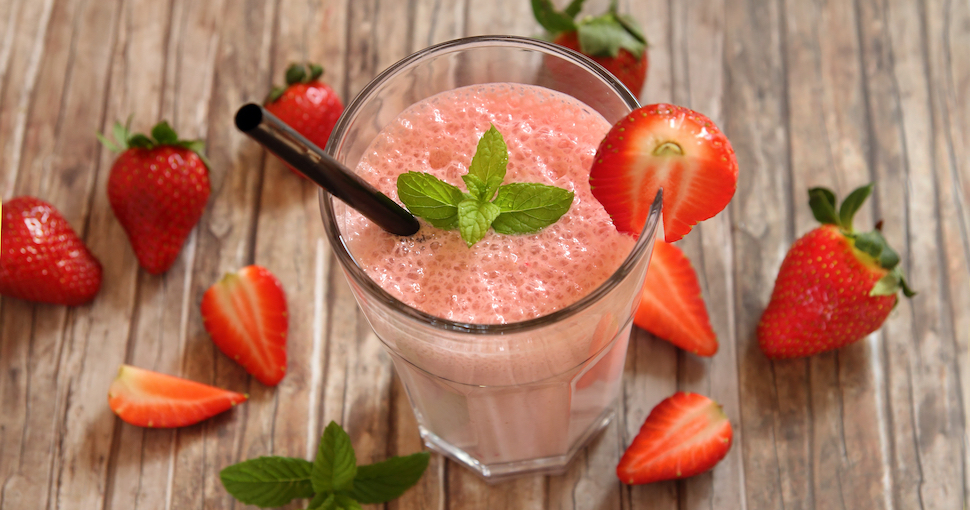 Image of a strawberry shake with strawberries around it.