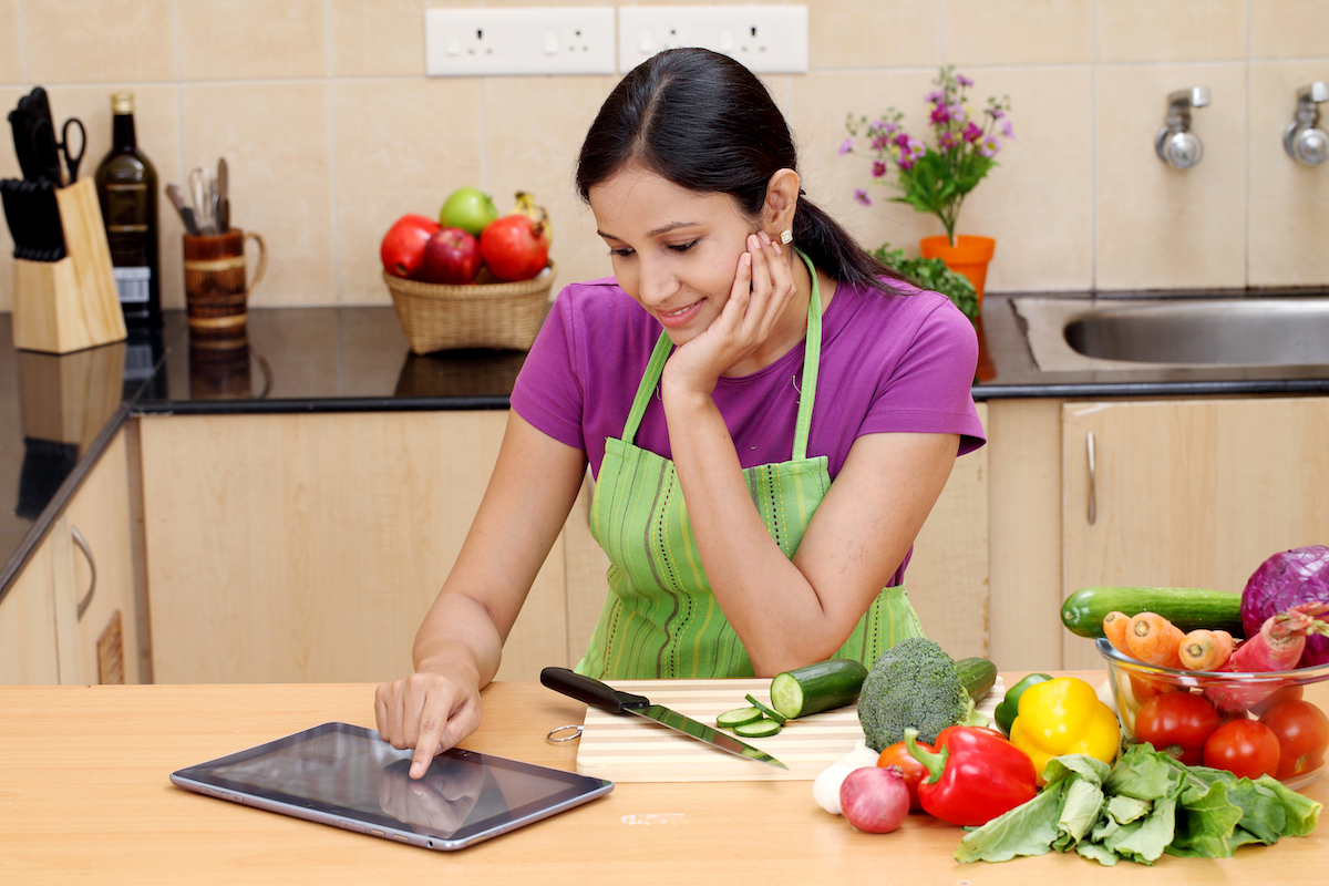 Woman using her Ipad and cooking a healthy meal